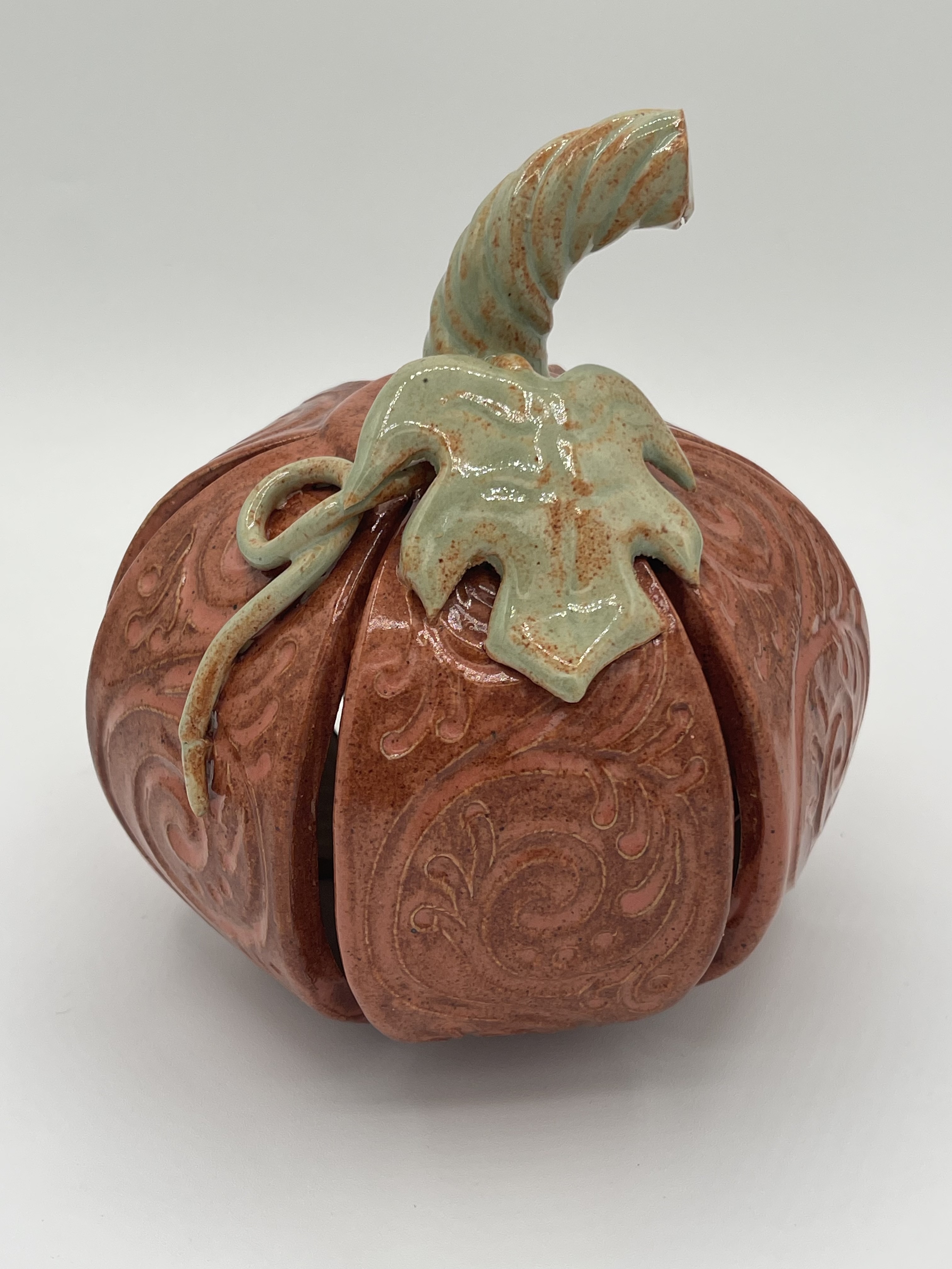Hand-sculpted orange ceramic pumpkin with decorative filigree, leaves, and curling stem